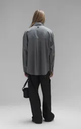 Camisa de manga larga en tejido twill color gris melange, con corte oversize. Presenta cuello clásico, cierre frontal con botones y tres bolsillos delanteros, uno de ellos oculto.