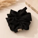 Colero de pelo tipo scrunchie, confeccionado en lino negro con diseño de volados y etiqueta de la marca Amalfi.