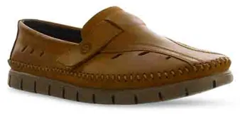 Zapato tipo mocasín de cuero color marrón, con diseño de costuras visibles en el contorno, perforaciones decorativas en el empeine y cierre con tira de velcro lateral. Cuenta con suela de goma estriada en tono gris oscuro.