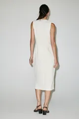 Vestido midi blanco sin mangas, con escote en V y costuras con ribetes negros a contraste. Cuenta con falsos botones decorativos en la parte delantera y una abertura central en el bajo.
