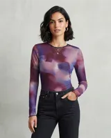 Body de manga larga confeccionado en tejido semitransparente con estampado abstracto en tonos violeta y azul. Presenta cuello redondo y terminaciones con ondas sutiles en los puños.