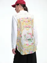 Camisa blanca de corte clásico con bordados florales en los hombros y detalles decorativos en los bolsillos frontales. Cuenta con cierre de botones y mangas largas.