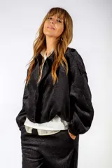 Campera corta de color negro con cierre frontal, cuello camisero y puños elásticos. Presenta un sutil estampado de textura animal print tono sobre tono.