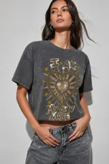 Remera corta de corte boxy y mangas cortas, con efecto de lavado ácido en color gris oscuro. Presenta un estampado frontal con el texto "I AM MY OWN MUSE" rodeando un corazón con detalles geométricos y estrellas en tonos dorados y violeta.