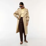 Gabardina larga color beige, con cuello solapa, doble botonadura frontal, trabillas ajustables en las muñecas y cinturón con hebilla. Presenta un corte recto y largo hasta la mitad de la pantorrilla.