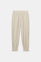 Pantalón bombacho color beige de tiro medio con cintura elástica, bolsillos delanteros y bajo acabado en puño con lazada.