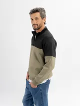 Buzo de felpa con diseño color block, combinando negro en la parte superior y beige en la parte inferior. Presenta cuello alto con cierre frontal parcial y puños elásticos.