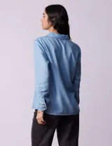 Camisa celeste de lyocell, con cuello a la base, escote en V y abertura central con botones. Tiene bolsillos aplicados en la parte delantera y mangas 3/4 regulables con presilla y botón.