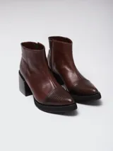 Botineta de cuero color suela, con diseño de punta fina y puntera texturizada con efecto reptil. Presenta una suela de madera clara con borde negro y cierre lateral interno.