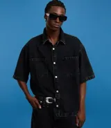 Camisa masculina de jeans negro con lavado marmolado, corte boxy, cuello inglés, manga corta, abotonada al frente y con dos bolsillos de parche en el pecho.