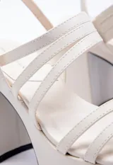 Sandalia de tacón alto color blanco, con plataforma y tiras finas sobre el empeine y agarre con hebilla en el tobillo.
