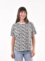 Remera de manga corta color beige con estampado de bananas en tonos amarillo, naranja y rosado.