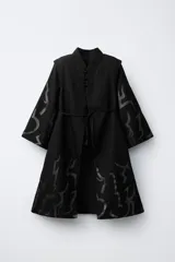 Capa de estilo oriental en color negro, con cuello mao, cierre frontal de alamares y mangas anchas. Presenta un estampado gráfico tonal en toda la prenda y un cinturón de cuerda trenzada ajustable en la cintura.