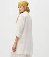 Salida de playa tipo túnica camisera blanca, con mangas 3/4, cuello camisero y cierre frontal con botones. Confeccionada en algodón certificado BCI.