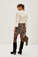 Falda corta tipo portafolio de gabardina liviana, color negro, con bordados florales y de ave en tonos dorados, rosados y morados. Posee un lazo lateral para atar.