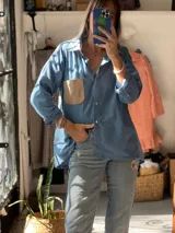 Camisa de corte oversize color celeste, confeccionada en una combinación de lino, lienzo y pana. Presenta cuello clásico, cierre frontal con botones y un bolsillo de parche en color beige en el pecho.