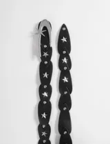 Cinturón de cuero sintético negro compuesto por piezas en forma de gota entrelazadas, decoradas con tachas metálicas en forma de estrella. Cuenta con una hebilla metálica plateada con diseño de luna creciente y estrella.