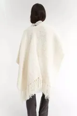 Ruana color crema tejida a mano, con cuello redondo y flecos en el ruedo.