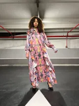 Vestido largo con estampado abstracto en tonos rosa, amarillo, negro y celeste. Presenta cuello redondo con volados y mangas largas con puños elásticos.