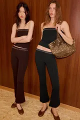 Pantalon negro de corte flare, confeccionado en tejido elastizado. Presenta tiro alto, cintura elastizada y detalle de tachas metálicas decorativas en la parte superior.