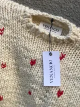 Sweater de lana merino color crema con pequeños corazones rojos bordados.