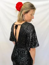 Mono corto de fiesta con lentejuelas negras, escote en V, mangas cortas acampanadas y espalda descubierta con lazo.