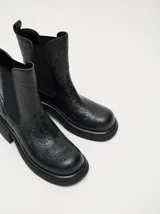 Bota tipo chelsea de cuero vacuno en color rojo con estampado floral grabado en negro. Presenta paneles laterales elásticos, suela de plataforma y taco cuadrado en color negro.