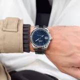 Reloj analógico Maserati Competizione con caja y malla de acero inoxidable plateado. Presenta una esfera azul con indicadores de hora, manecillas luminiscentes y ventana de fecha a las tres en punto. El bisel estriado aporta un toque distintivo al diseño.