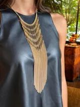 Collar de diseño llamativo compuesto por múltiples capas de cadenas doradas y barras metálicas verticales que descienden en un fleco largo y fluido.