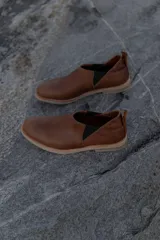 Zapatos tipo chelsea de cuero color marrón, con paneles elásticos laterales y suela plana de goma.