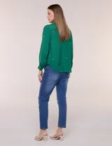 Camisa de estilo boho, color verde, con cuello camisero, escote en V y botonadura frontal con botones perlados. Cuenta con una pechera con bordados geométricos y florales a contraste, mangas largas abullonadas con puños abotonados y delicados bordados dispersos.
