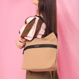 Cartera grande color tostado con detalles en negro, confeccionada en tela impermeable. Cuenta con un amplio compartimento principal, bolsillo frontal con cierre oculto, bolsillo trasero con cierre, asa corta de mano y correa larga desmontable.