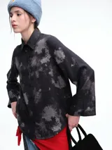 Camisa oversize de lyocell con estampado orgánico efecto lavado. Presenta cuello clásico, cierre frontal con botones, mangas amplias con puños anchos y un diseño de corte relajado con ruedo asimétrico, siendo más largo en la parte posterior.