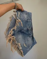 Short de denim azul con efecto desgastado, roturas extremas y flecos en los laterales.