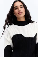 Buzo de punto con diseño bicolor en bloques ondulados de color blanco y negro. Presenta cuello alto, manga larga y una estructura de tejido marcada con calce relajado.