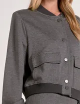 Camperita tipo bomber color beige claro, con cuello redondo acanalado, cierre frontal con broches metálicos y bolsillos delanteros con tapa. Los puños y el bajo son acanalados.