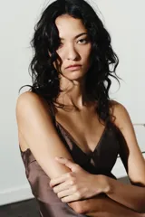 Vestido midi marrón satinado con escote en V, tirantes finos regulables, espalda descubierta con lazo y bajo asimétrico con encaje a tono.