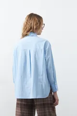 Camisa de corte relajado y diseño clásico, confeccionada en tela de algodón color celeste. Presenta cuello tradicional, cierre frontal con botones y mangas largas con puños rectos.