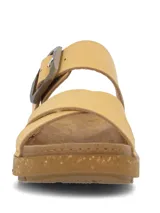 Sandalia de color amarillo claro con diseño de doble tira cruzada en el empeine, una de ellas ajustable con hebilla grande. Suela de plataforma baja con textura tipo corcho.
