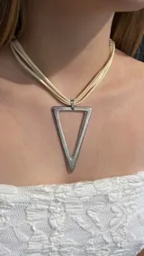 Gargantilla tipo choker con dije de triángulo metálico plateado, sostenido por múltiples tiras de cuero sintético en color beige.