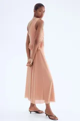 Vestido largo sin mangas de punto liviano, color rosado, con escote de pico pronunciado y ribetes de volado. Presenta volados de doble capa bajo el busto que se extienden por la cintura trasera. El vestido es forrado.