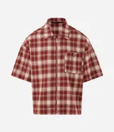 Camisa de franela de algodón con diseño a cuadros en tonos rojo y beige, de corte holgado relaxed, mangas cortas, cuello tradicional y cierre frontal con cremallera. Cuenta con un bolsillo aplicado en el pecho con detalle de botón metálico.