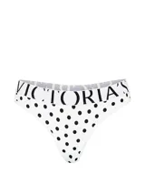 Tanga de tiro bajo confeccionada en microfibra blanca con estampado de lunares negros y cintura elástica con el logotipo de la marca.