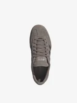 Championes Adidas modelo Handball Spezial de perfil bajo, confeccionados en gamuza color marrón topo con las clásicas tres tiras y detalles metalizados en tono plateado, inscripción lateral en relieve y suela de caucho translúcido.
