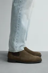 Bota estilo Chelsea de piel con acabado serraje color beige, con elásticos laterales para facilitar el calce, horma redonda y suela a tono con ligero tacón.