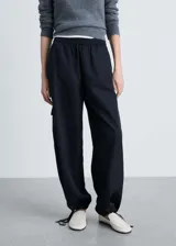 Pantalon de corte recto y tiro medio, confeccionado en tejido técnico de poliéster. Presenta cintura elástica, bolsillos laterales y bolsillos de parche con solapa en las piernas. El bajo cuenta con un sistema de fruncido regulable.