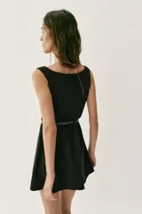 Vestido corto negro sin mangas, con escote en pico profundo y falda con pliegues. Incluye un cinturón fino de cuero sintético con hebilla metálica dorada en la cintura. Cierre lateral con cremallera oculta.