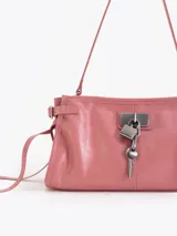 Bandolera de cuero vacuno color marrón con acabado brillante. Presenta un diseño estructurado con herraje metálico tipo candado y llave colgante en el frente, además de detalles de tiras laterales. Incluye correa de hombro y cierre superior.