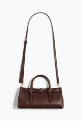 Cartera bandolera rectangular de color marrón, con diseño alargado y asas cortas de mano. Incluye un detalle de tira decorativa con hebillas metálicas en la parte frontal y herrajes dorados.