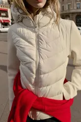 Cazadora acolchada color marrón con capucha ajustable, cuello subido y cierre frontal de cremallera. Presenta diseño combinado con mangas largas de tejido liso y cuerpo acolchado con costuras en chevrón, además de bolsillos laterales con cierre invisible.